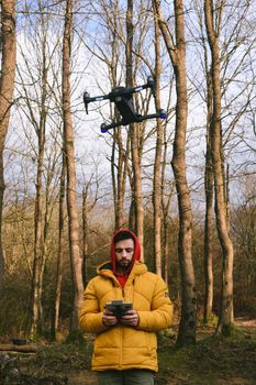A man operates a drone in a serene forest, capturing nature's beauty in winter.