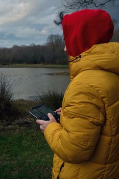 A person in a yellow jacket uses a drone controller by a lake in İstanbul, Türkiye.