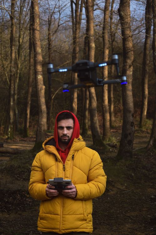 Free A man in a yellow jacket controls a drone in a serene autumn forest setting. Stock Photo