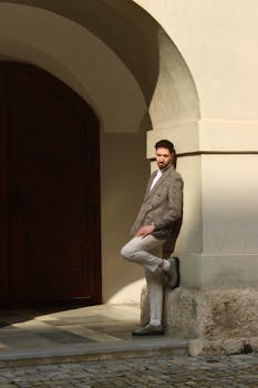 A fashionable man in a blazer poses in a sunlit archway in Graz, Austria.