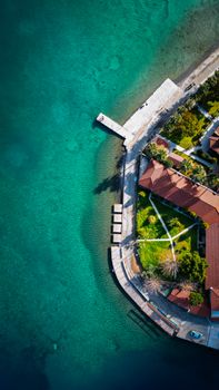 A stunning aerial view of a coastal park with red-roofed buildings and clear turquoise waters.