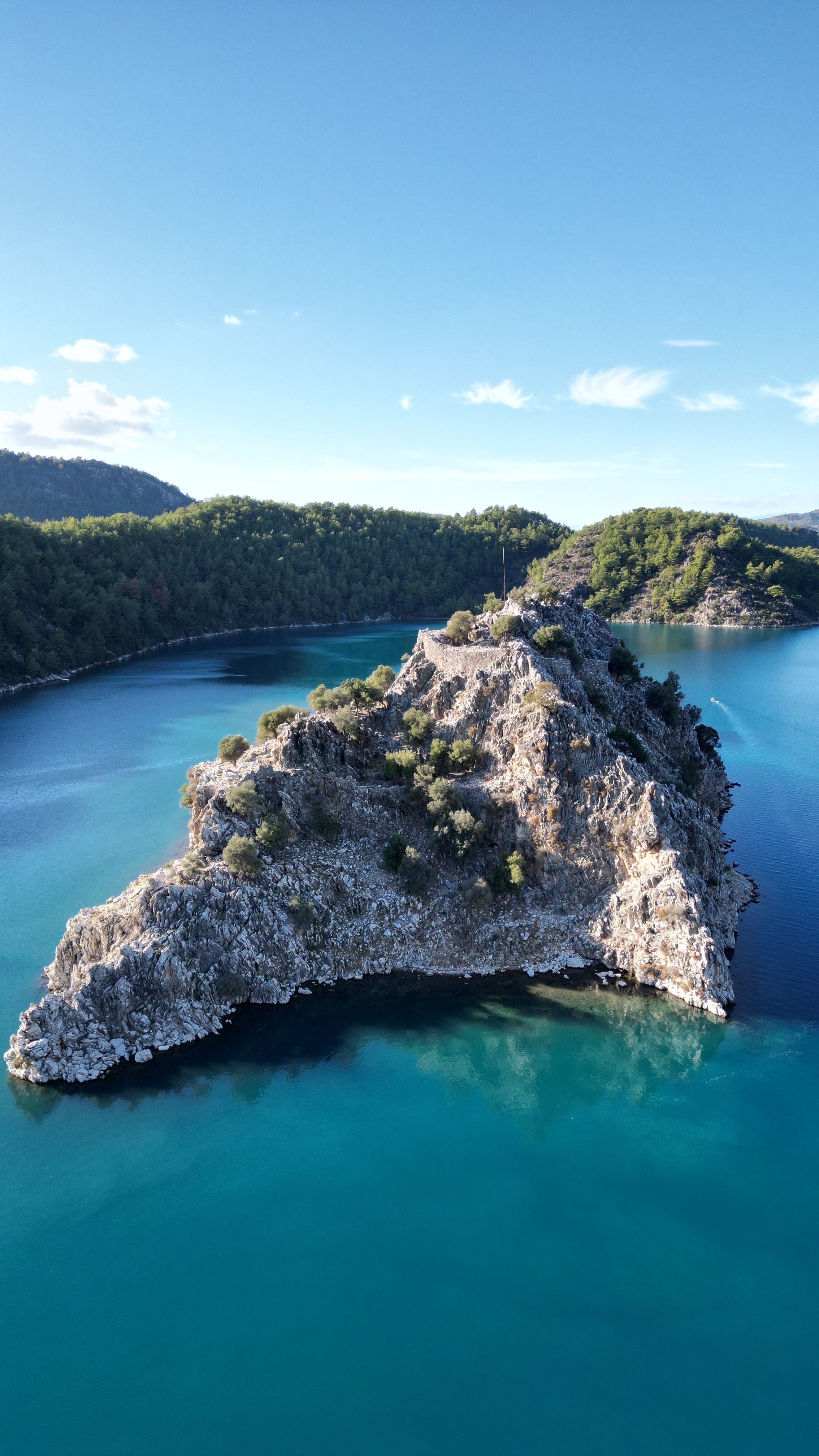 A stunning aerial view of a rocky island surrounded by turquoise water and lush greenery.