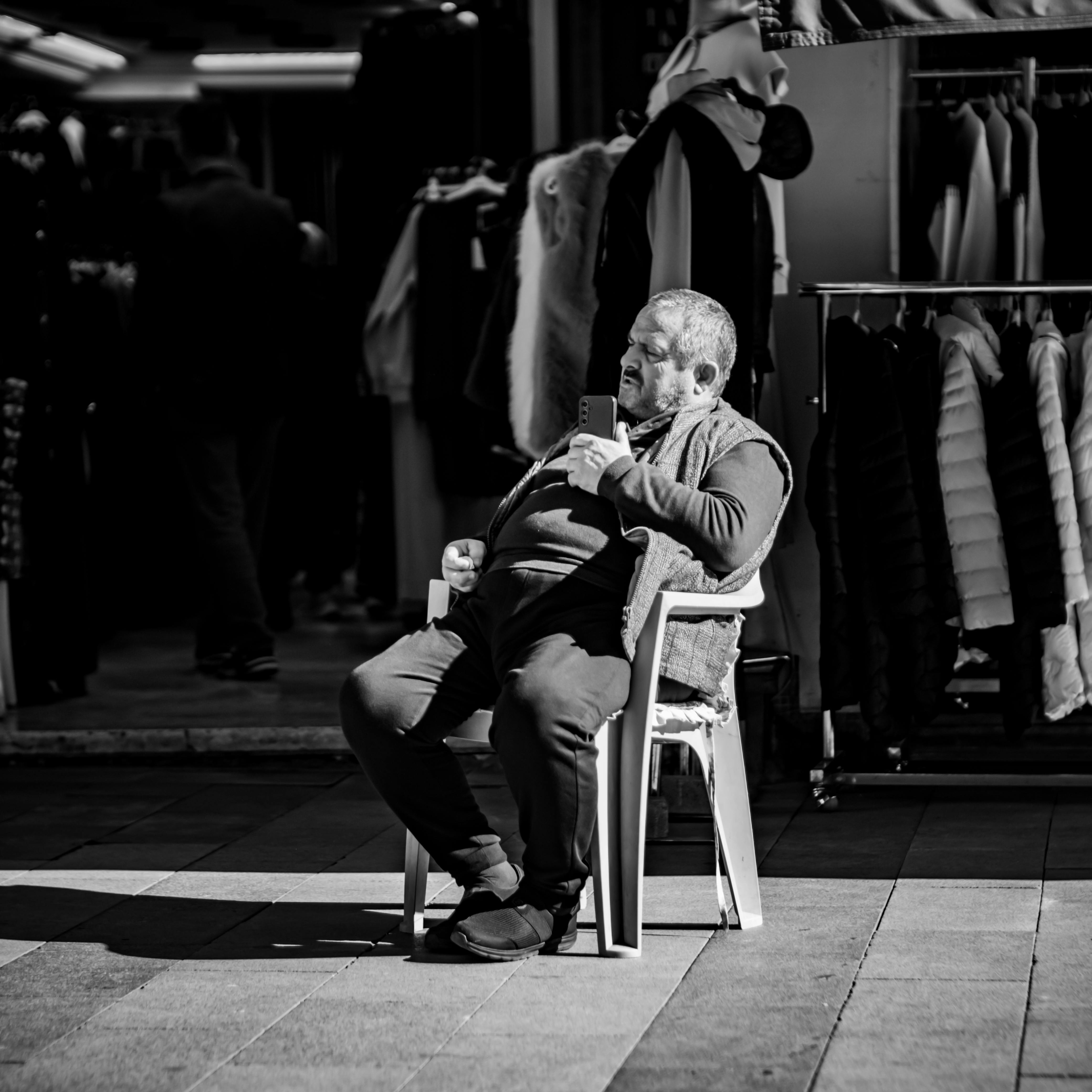 grátis Fotografia espontânea em preto e branco de um homem sentado ao ar livre com um smartphone, capturando uma cena de rua. Foto profissional