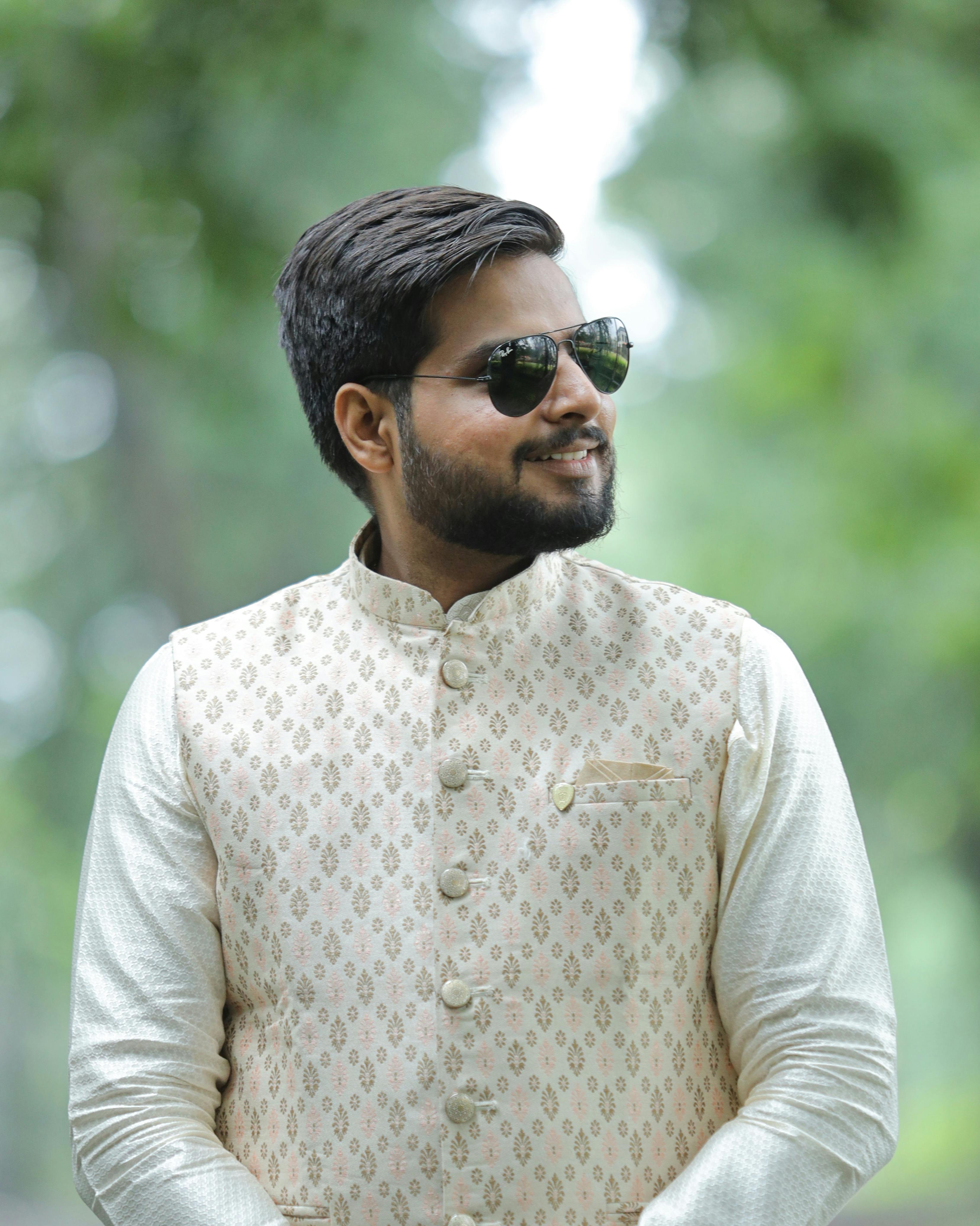 Portrait of a stylish man in sunglasses and traditional kurta standing outdoors on a sunny day.