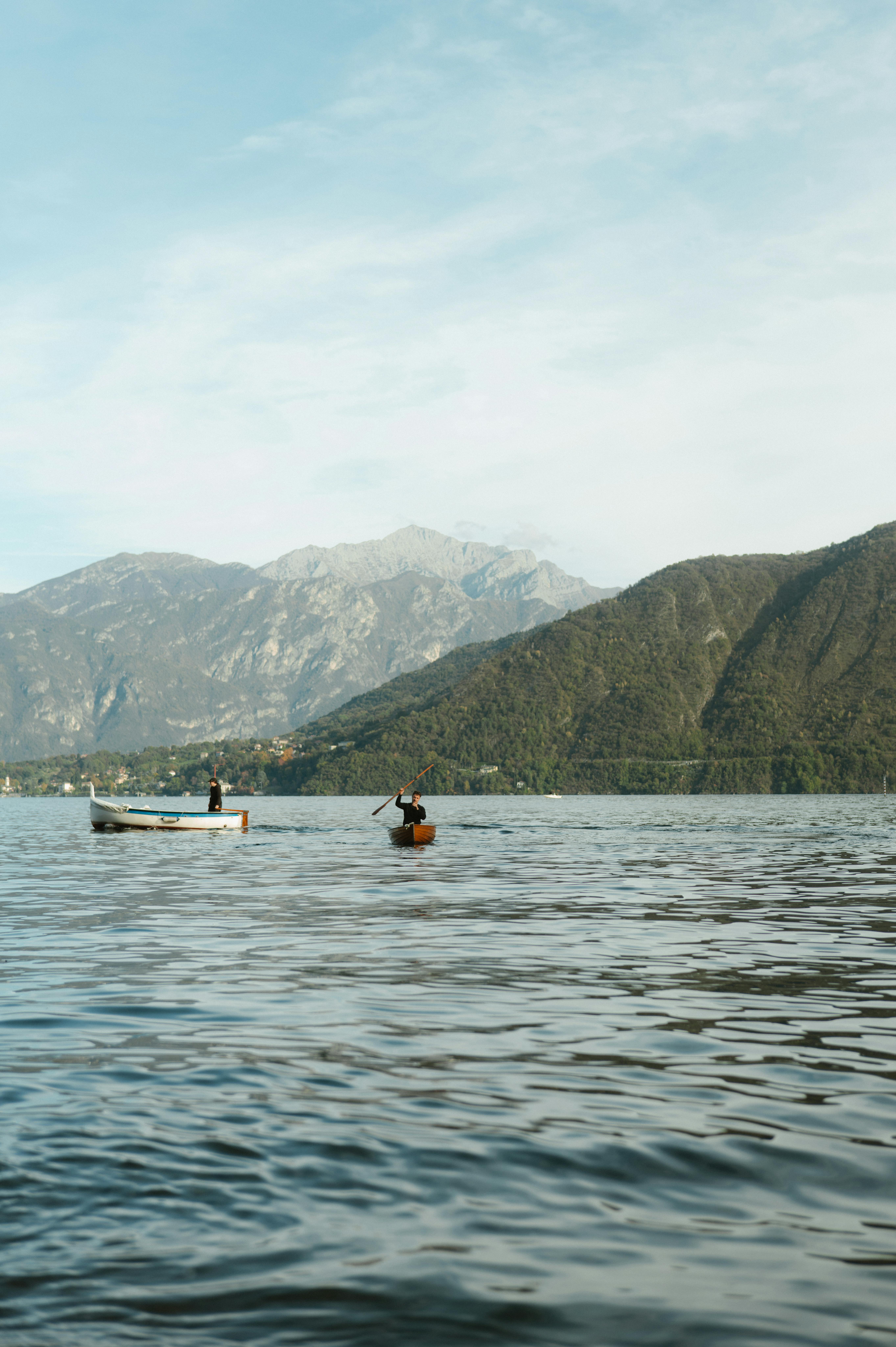 Tranquil evening view of individuals canoeing on a lake with mountainous backdrop.