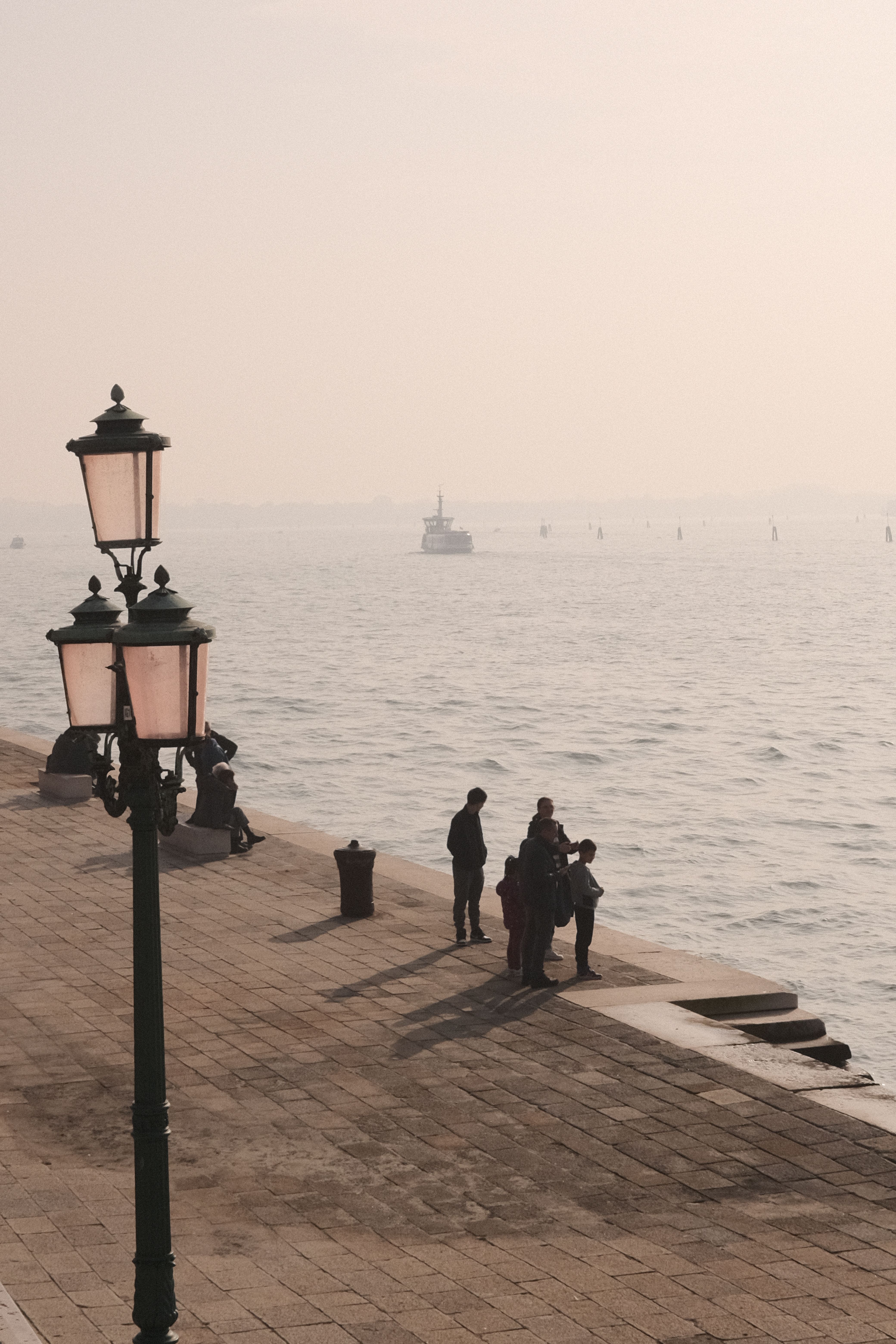 A family enjoys the peaceful morning by the Venetian waterside with classic lamp posts.