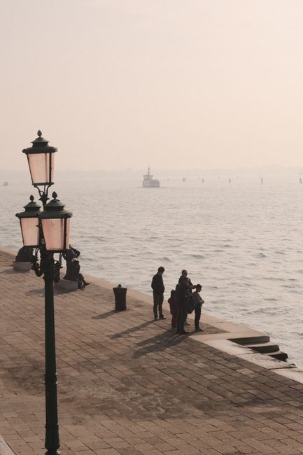 A family enjoys the peaceful morning by the Venetian waterside with classic lamp posts.