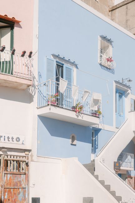 A charming pastel blue Mediterranean-style house with balconies and floral decor.