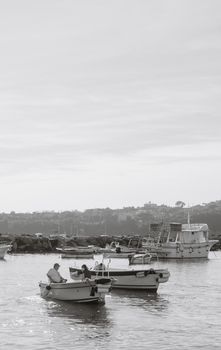 Two people fishing on a calm day in small boats near a rocky shore.