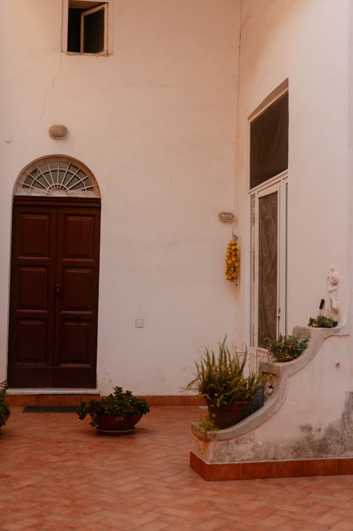 Free A cozy, rustic courtyard featuring a classic wooden door and vibrant potted plants. Stock Photo