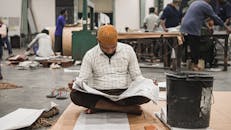 Man Reading Newspaper in Busy Workshop Environment