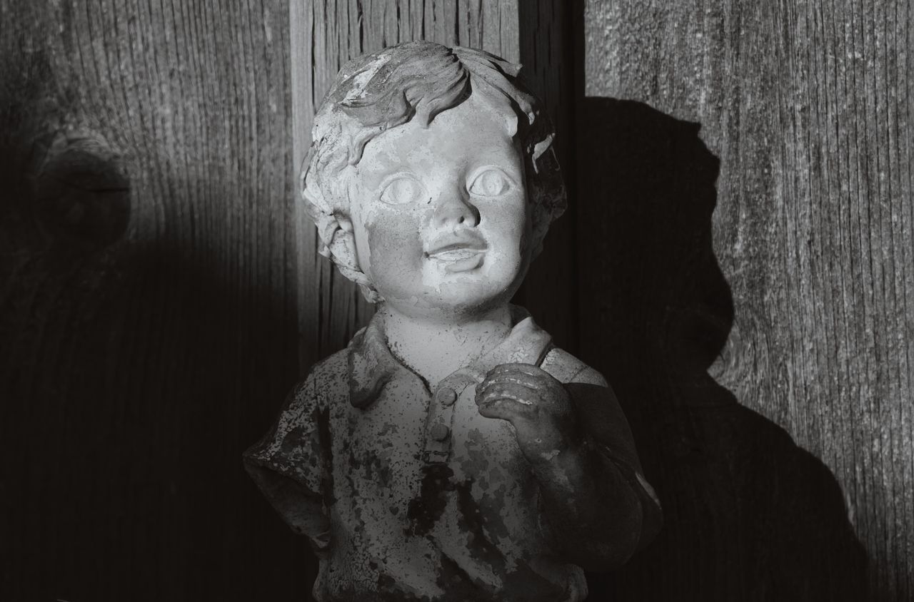 a black and white image of a child sculpture casting a shadow on a woo