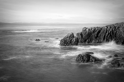 A calming black and white coastal scene with rocky formations and gentle waves.