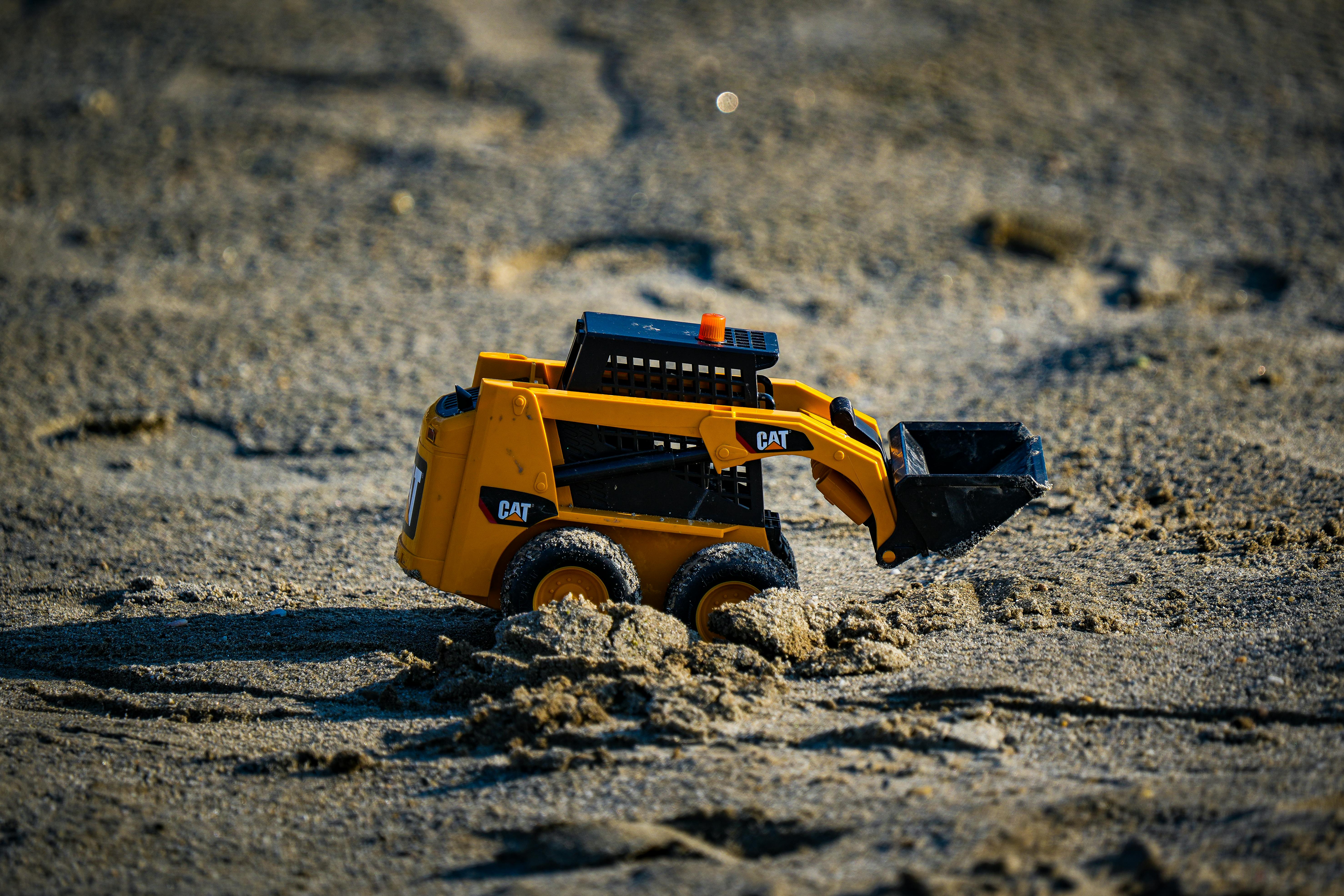 Gratuit Une mini-excavatrice jaune, jouet à jouer, creuse dans le sable sous un soleil éclatant. Photos