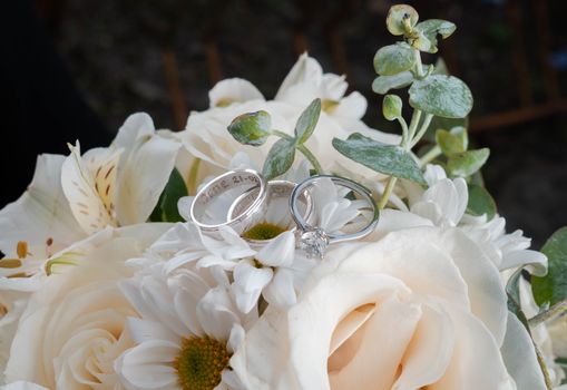 Close-up of wedding rings elegantly placed on a white floral bouquet, symbolizing love and commitment.
