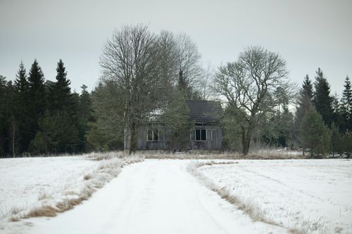 Free A deserted wooden cabin amidst a snowy field and forest during a winter day. Stock Photo