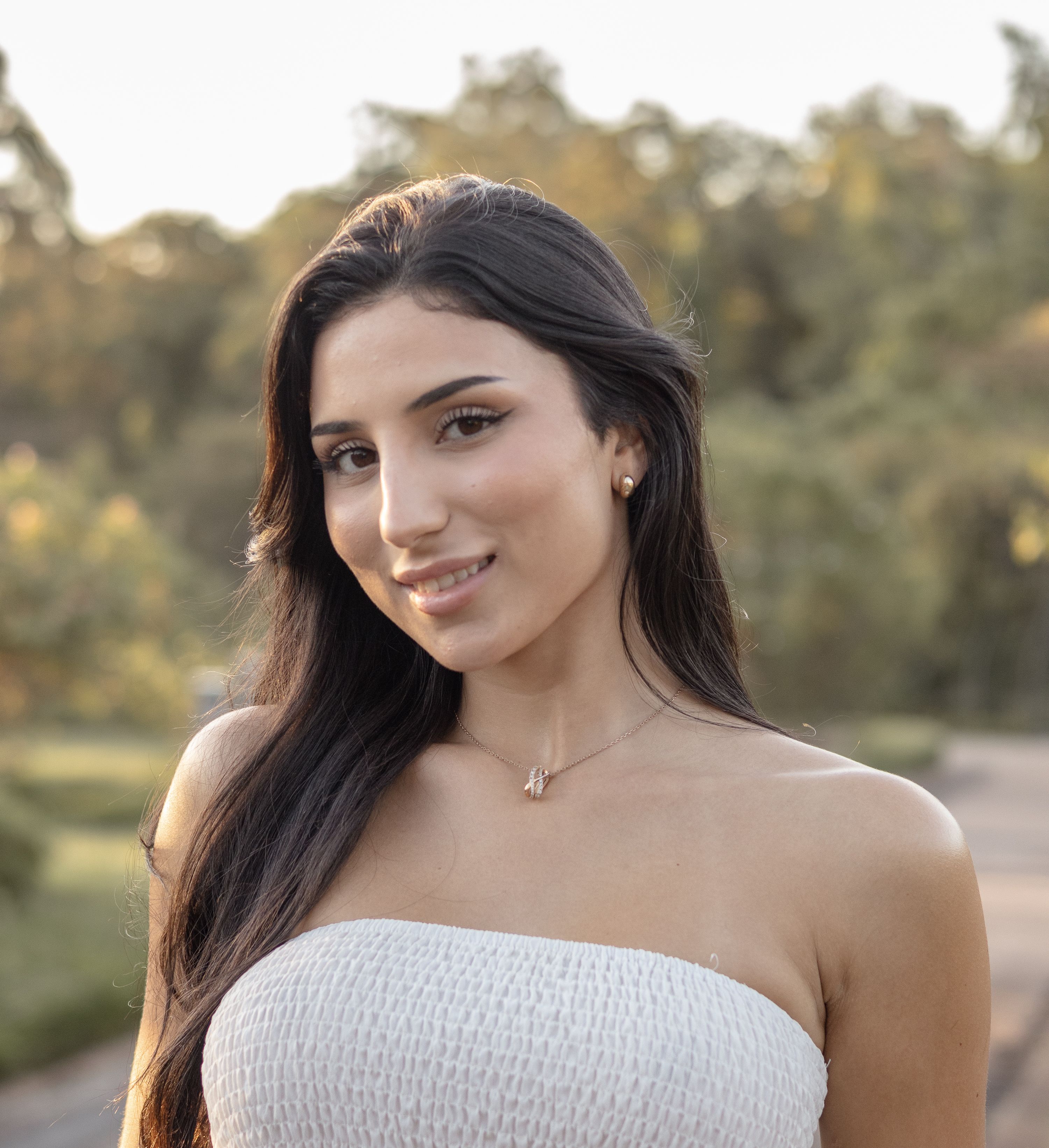 Portrait of a young woman smiling outdoors in a natural setting during the day.