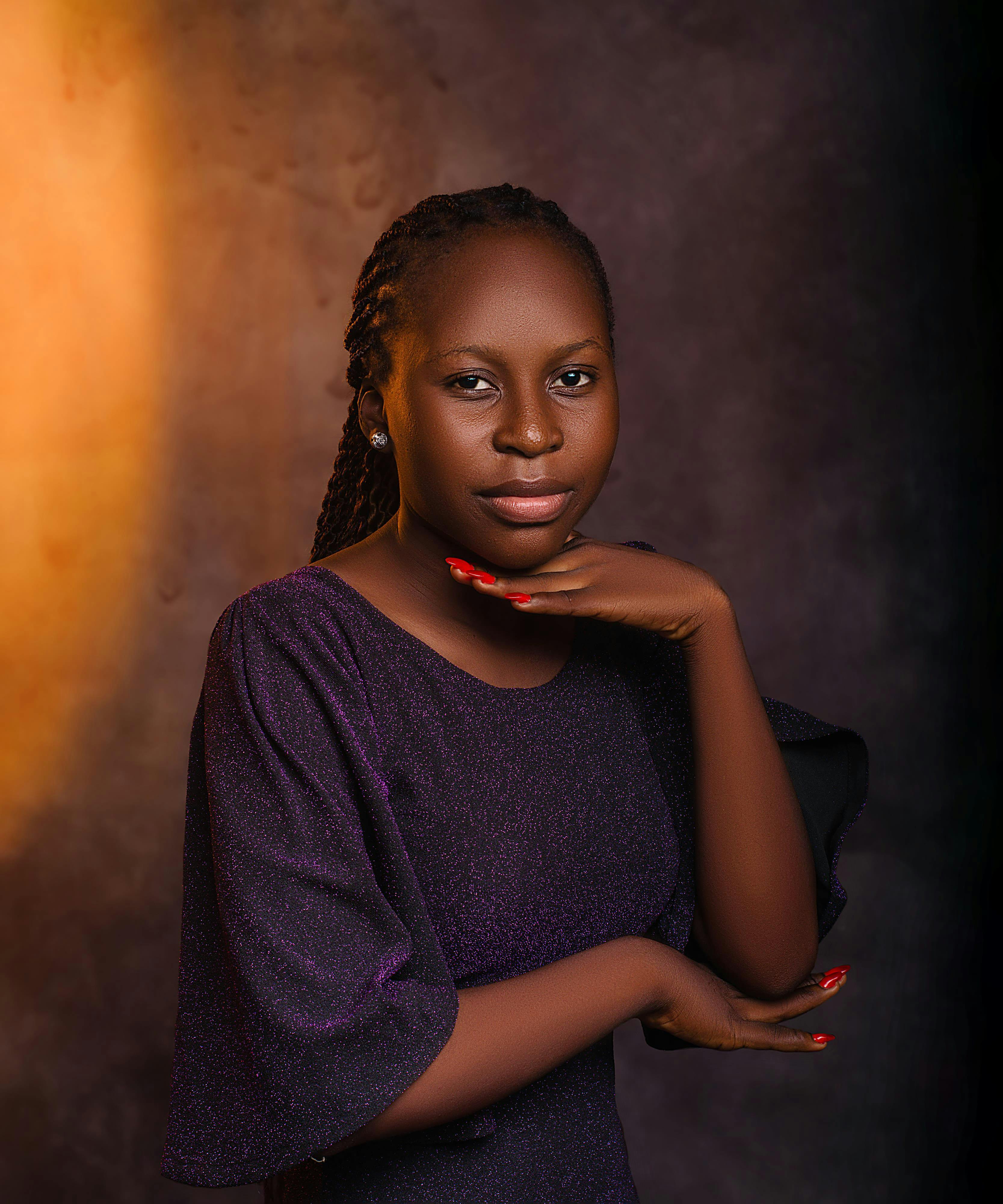 A woman poses gracefully in a studio portrait with soft lighting and a warm background.