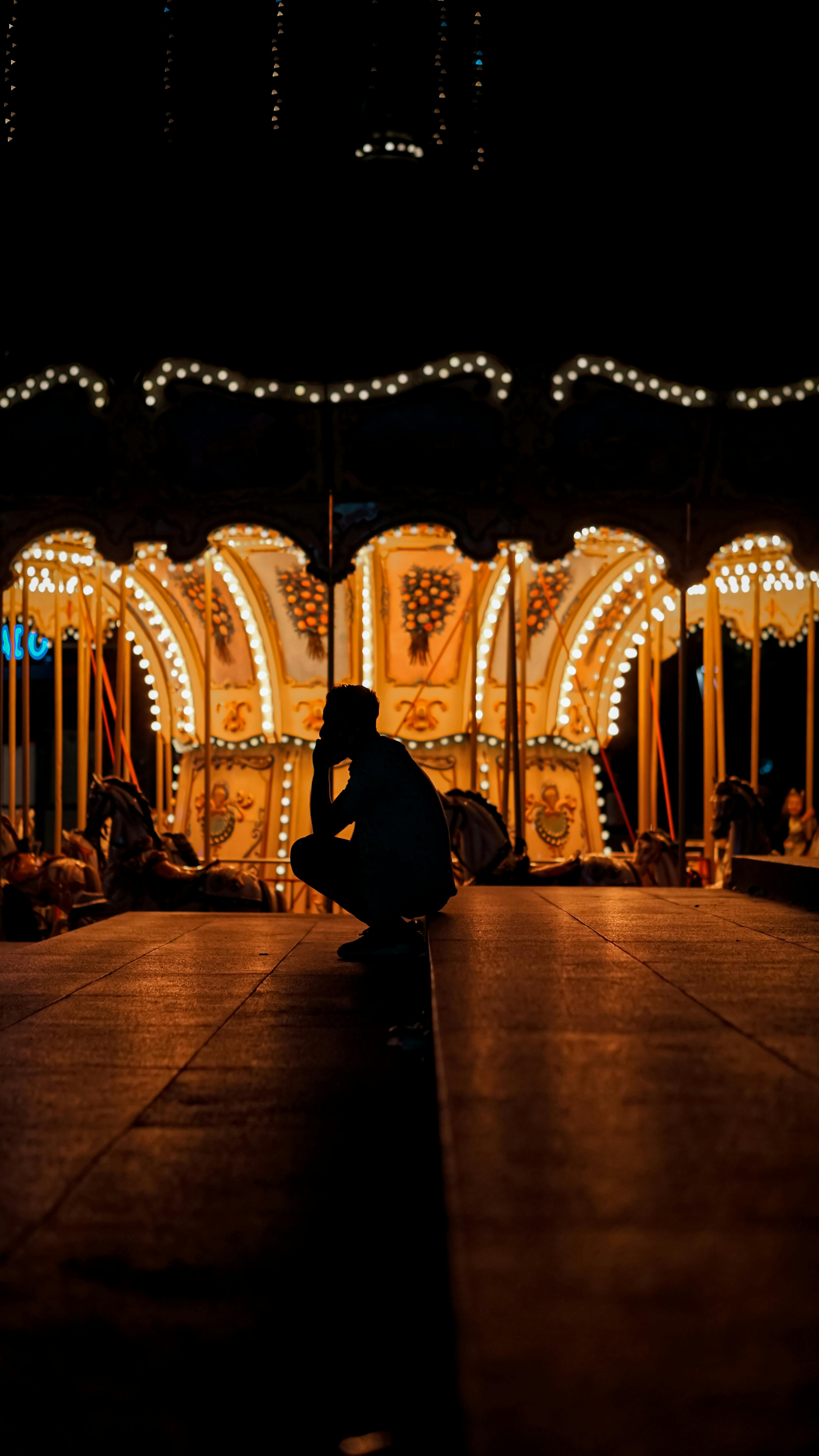 Gratis Silueta de una persona agachada frente a un carrusel brillantemente iluminado por la noche. Foto de stock