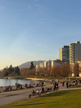 Crowds enjoying a sunny day at Vancouver's beachfront with city skyline in view.