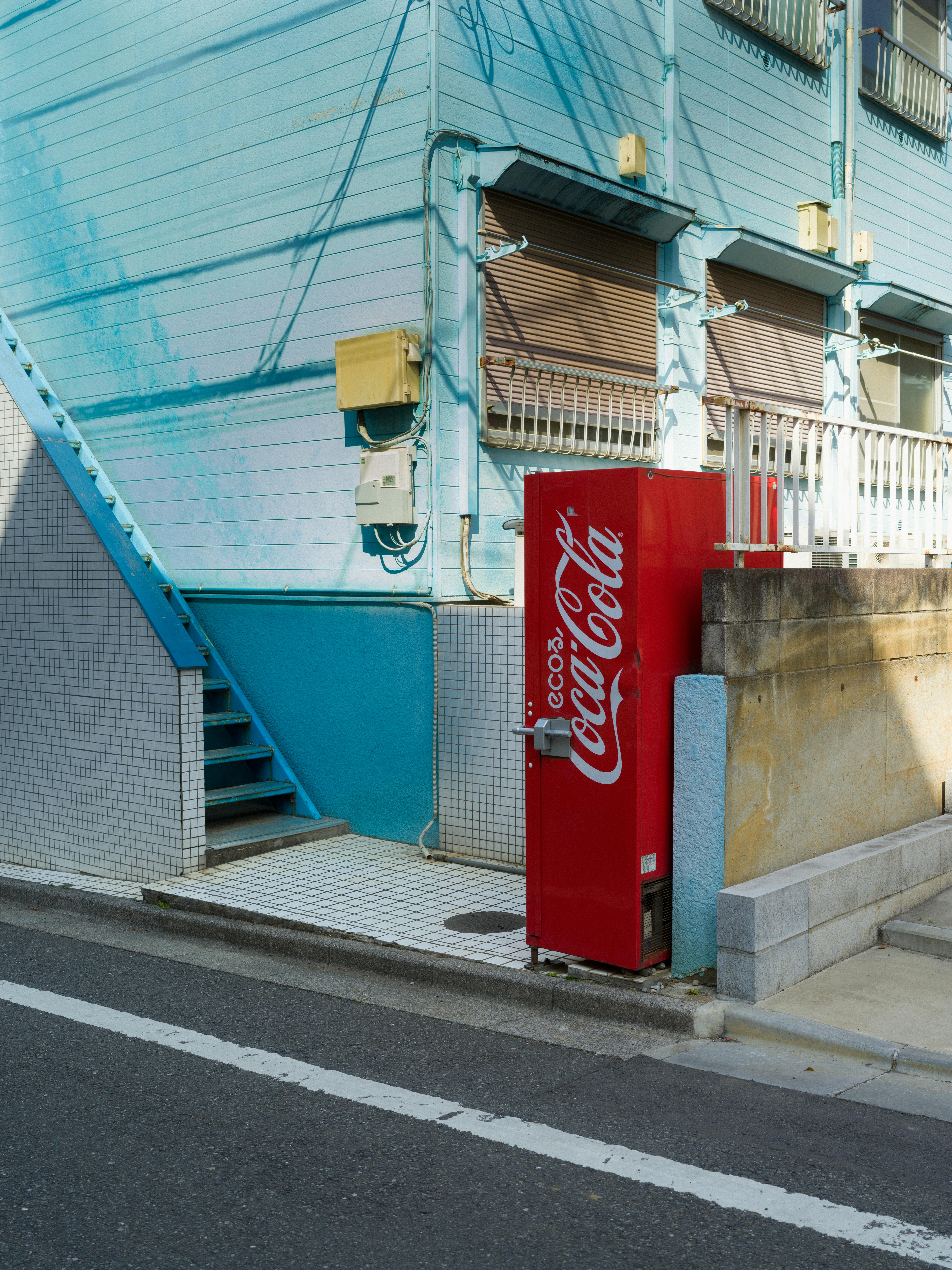 Free Red Coca-Cola vending machine against blue building in Tokyo, Japan street. Stock Photo