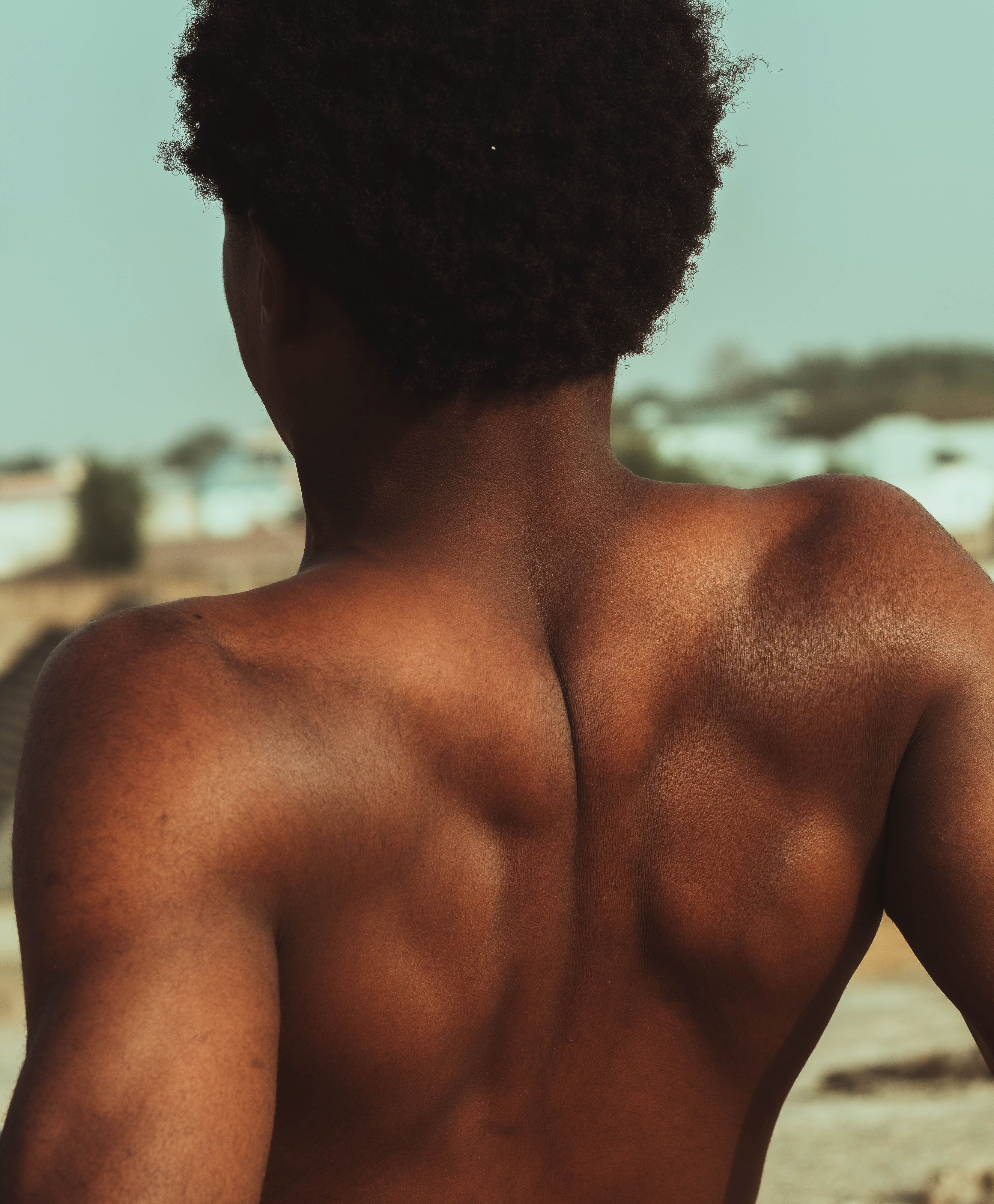 A strong and athletic male standing outdoors, showcasing defined back muscles.