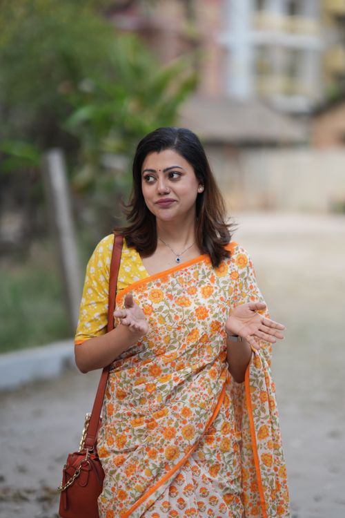 Free A woman walks along a path wearing a vibrant floral saree and carrying a red purse. Stock Photo