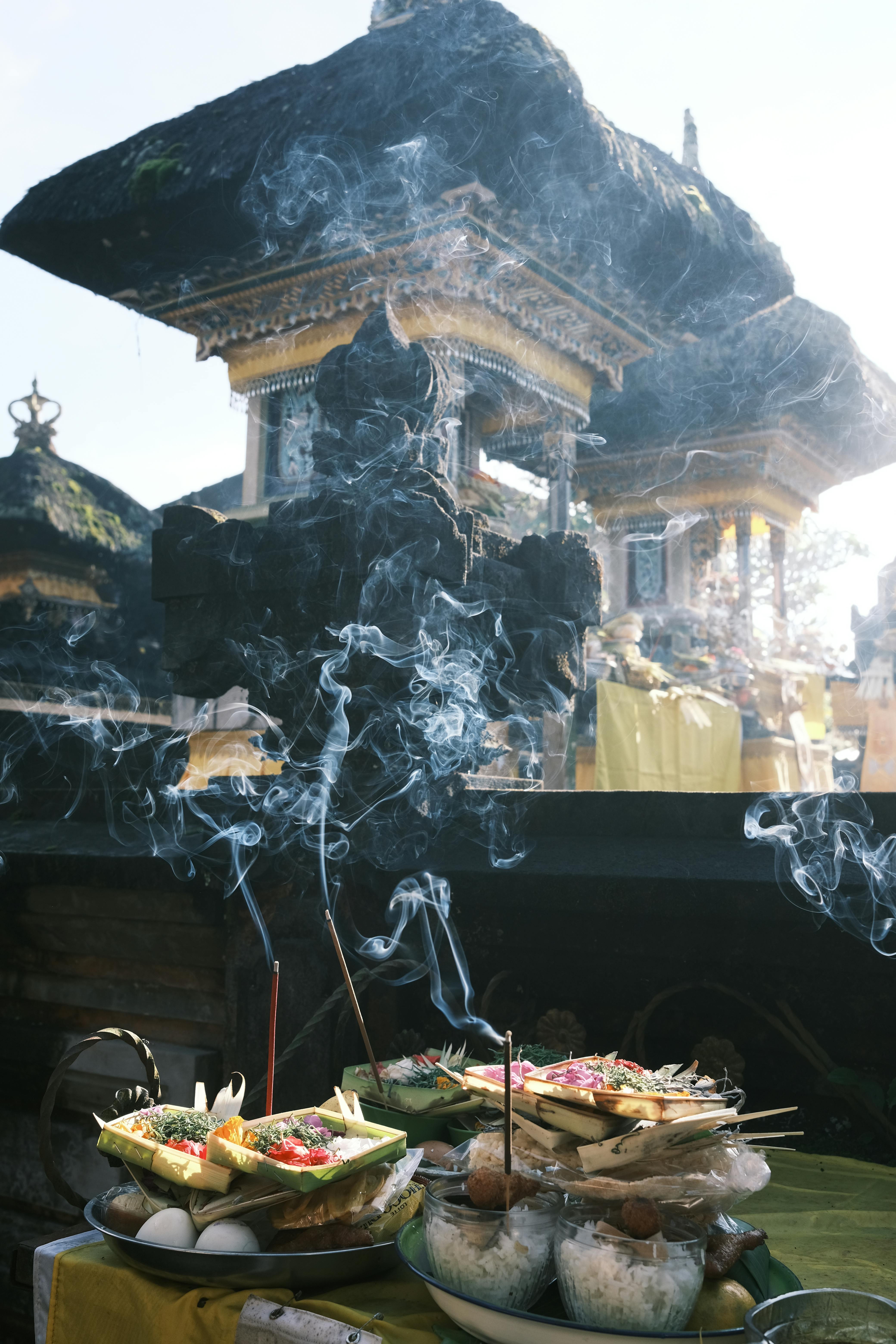 Canang sari offering with frangipani petals, rice, and burning incense placed at a Balinese Hindu temple shrine in Bali