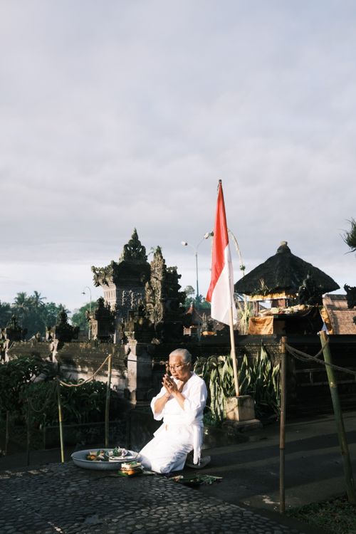 Free Elderly man performs ritual at a Balinese temple with Indonesian flag in view. Stock Photo