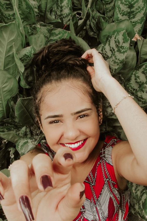 Free Happy woman lying in lush green foliage, reaching towards the camera with a joyful smile. Stock Photo