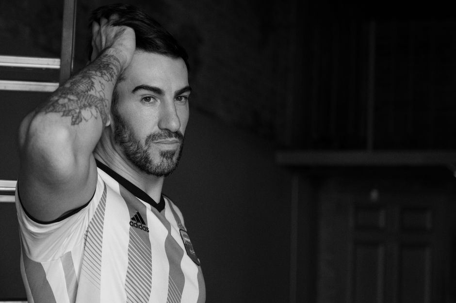 Black and white portrait of a man wearing an Argentine football jersey, looking thoughtful.