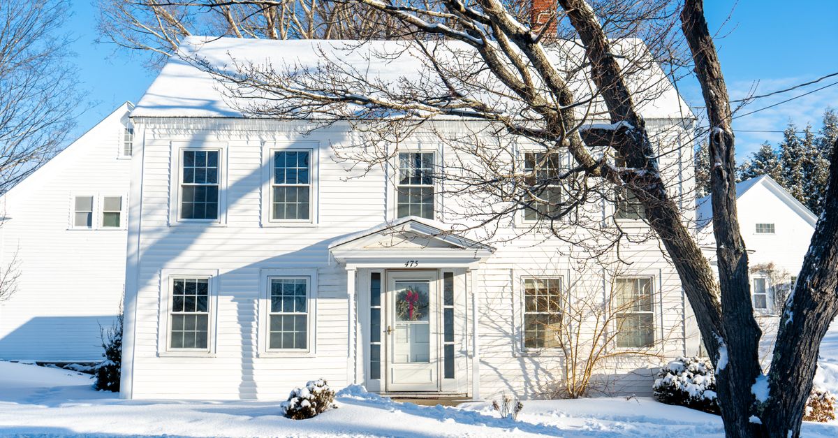 Beautiful colonial-style house covered in snow during a bright winter day, showcasing classic architecture.