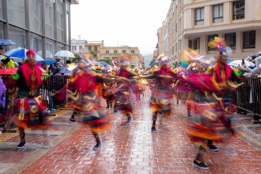 Colorful dancers in traditional costumes performing at a lively street festival on a rainy day.