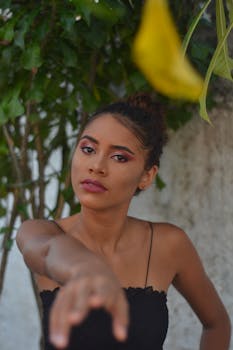 A woman with makeup poses outdoors with an outstretched arm, capturing a candid moment.
