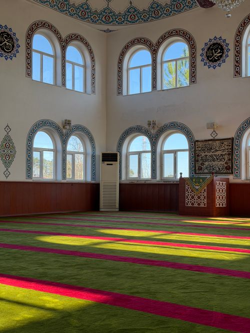 Free Peaceful interior of a Turkish mosque with sunlight casting shadows on a vibrant carpet. Stock Photo
