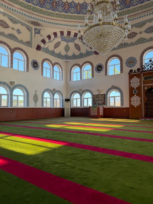 Free Sunlit mosque interior with colorful carpet and ornate decorations in Türkiye. Stock Photo