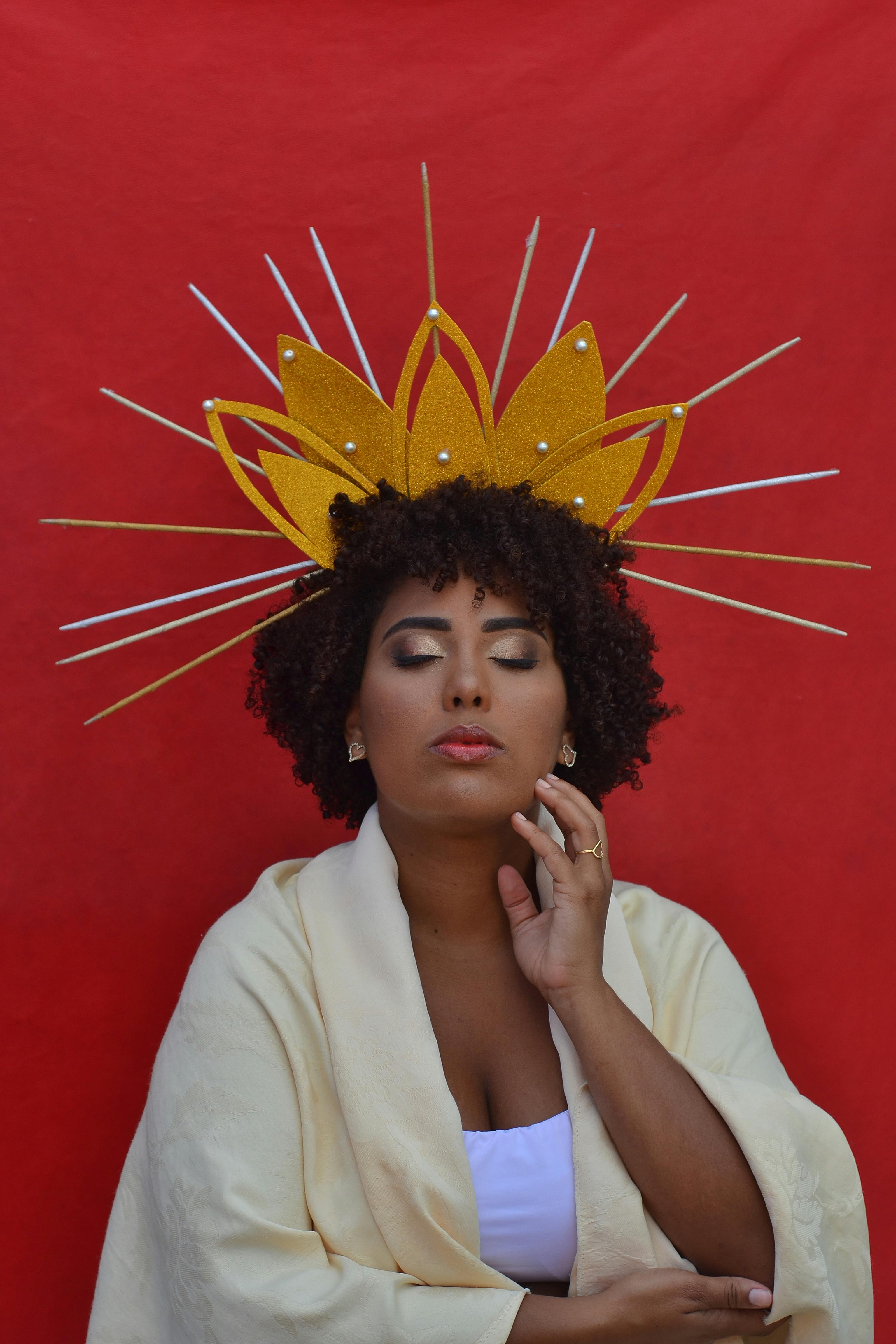 A serene woman with a striking headpiece against a vivid red backdrop.