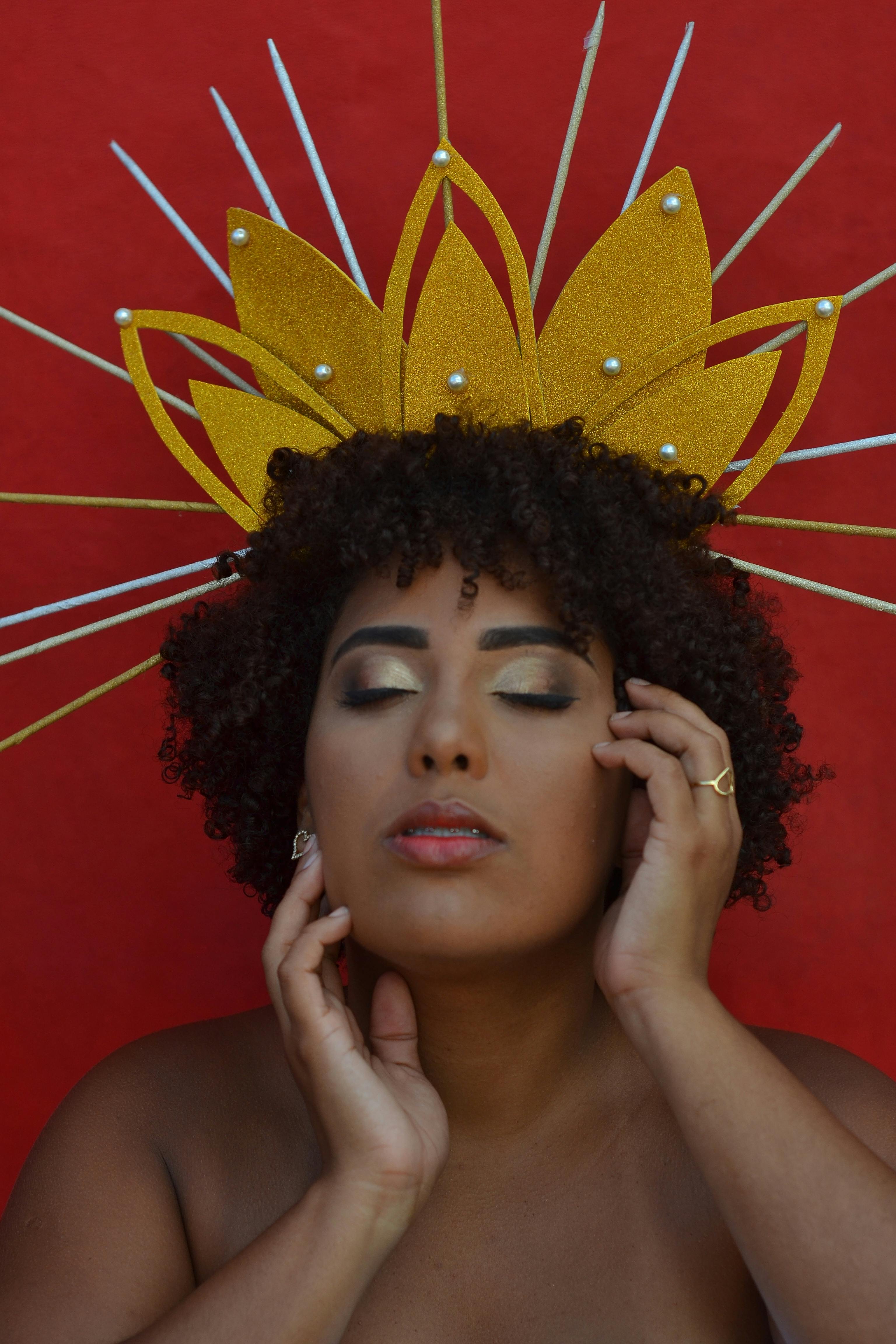 Portrait of a woman with curly hair wearing a golden headpiece, with serene expression.