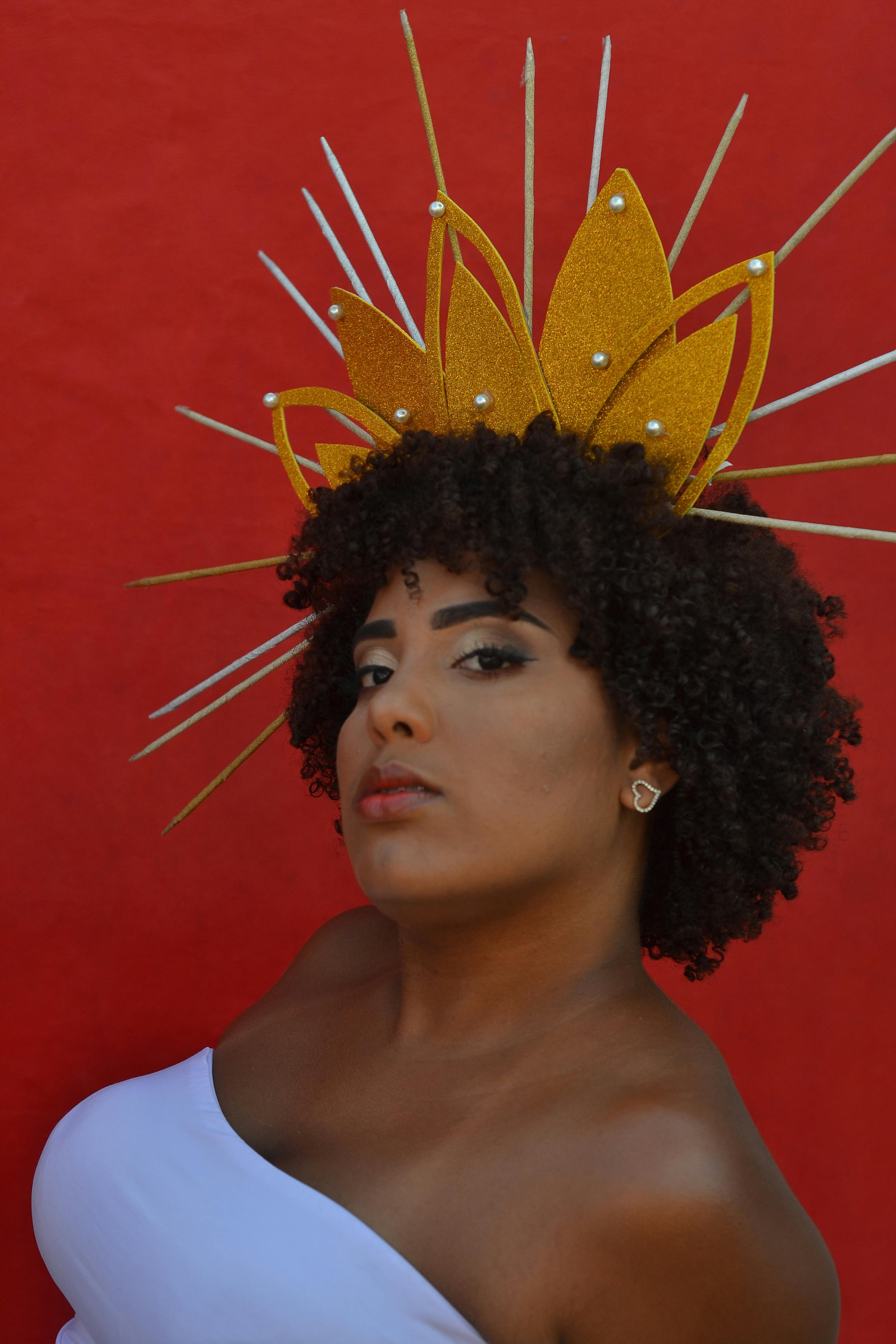 Stunning portrait of a woman wearing a golden artistic headdress posing against a vivid red backdrop.
