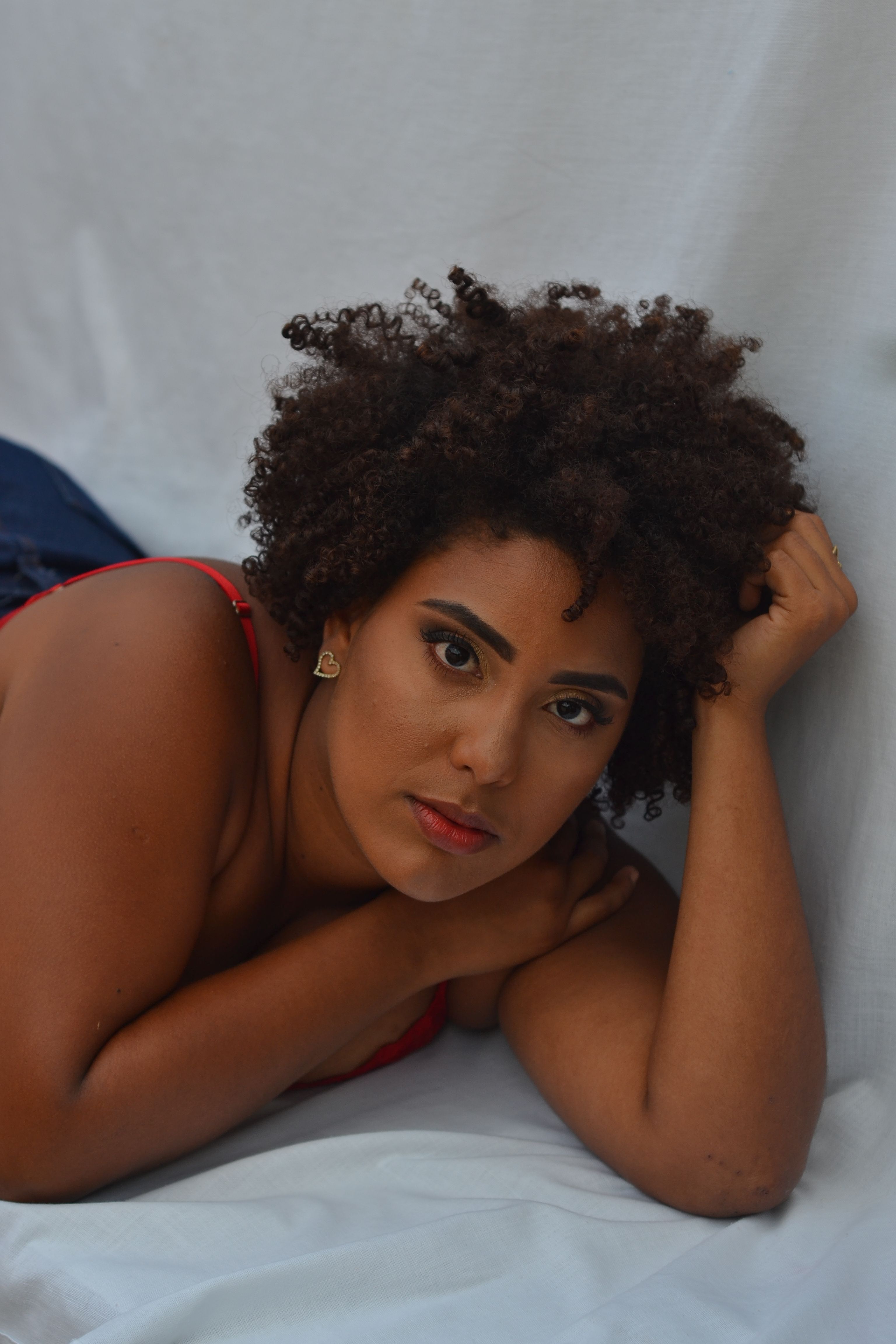 Close-up portrait of an adult woman with curly hair lying on a white sheet, gazing at the camera.