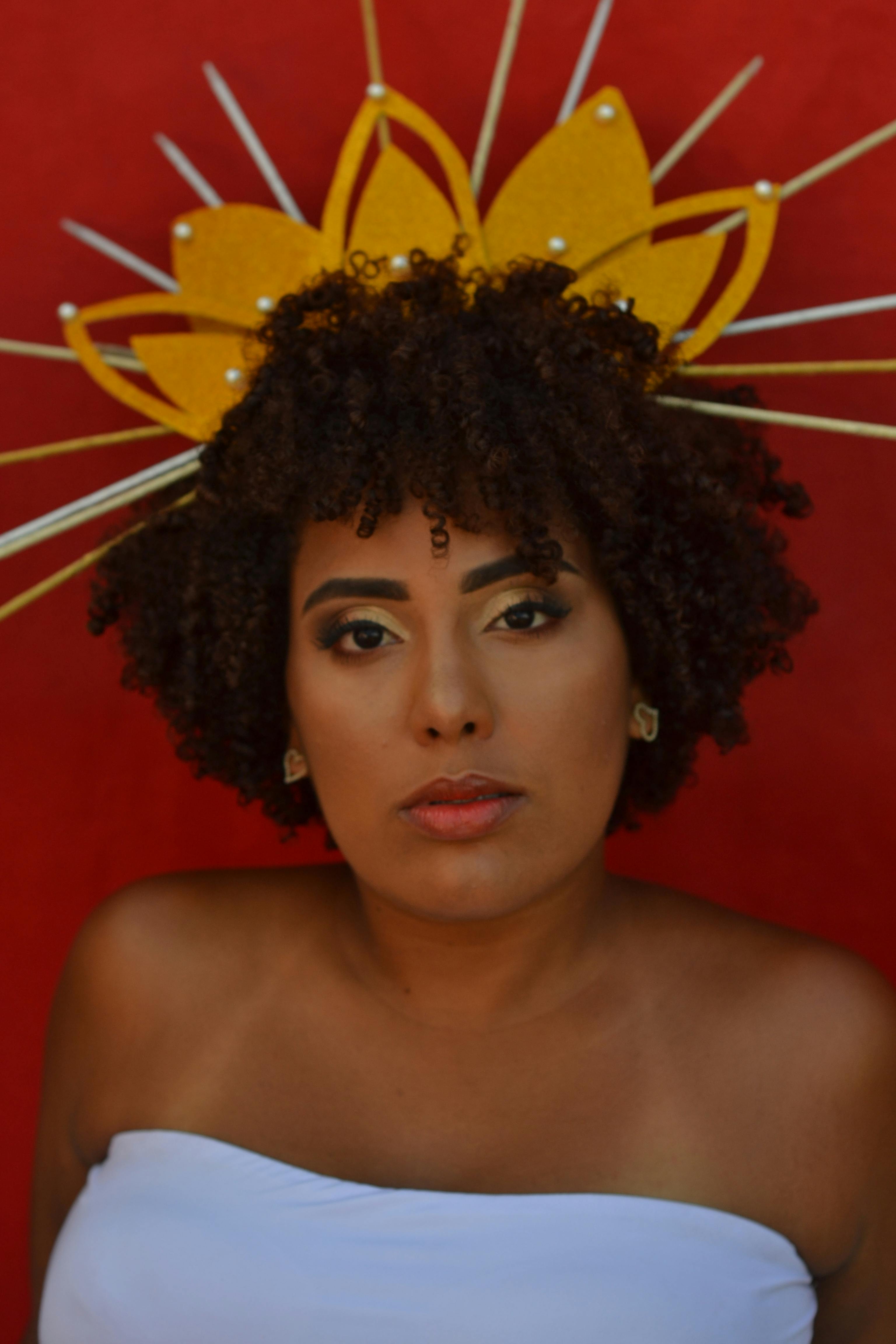 Striking portrait of a woman wearing an ornate yellow headpiece against a red background.