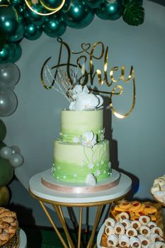 Green two-tier birthday cake with white orchids and gold text decoration.
