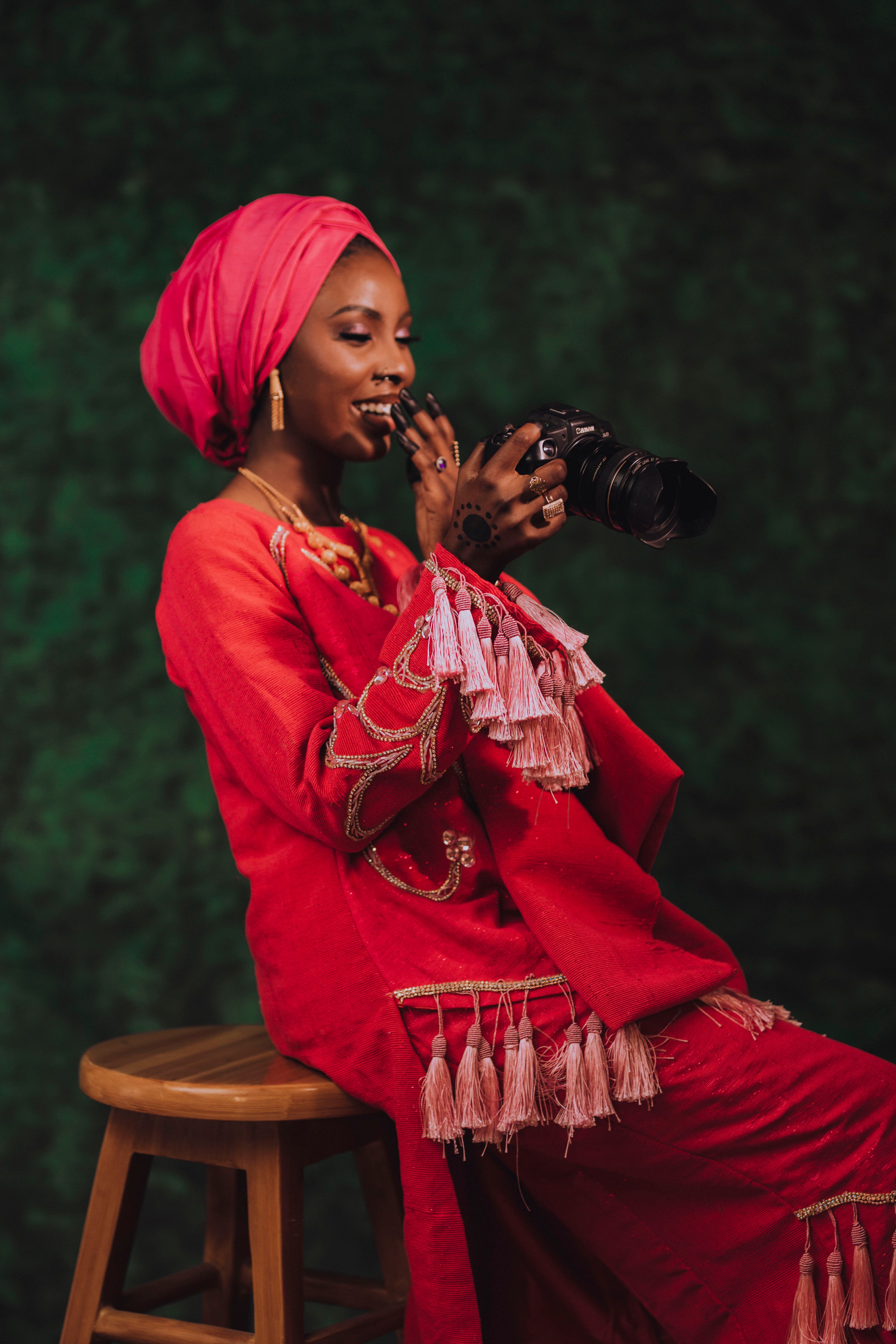 Woman in vibrant red traditional dress joyfully holding a camera indoors.
