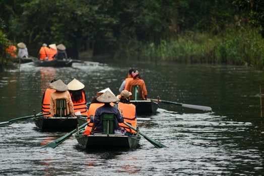 Group enjoying a peaceful boat ride on a lush Asian river, wearing traditional hats and life vests.