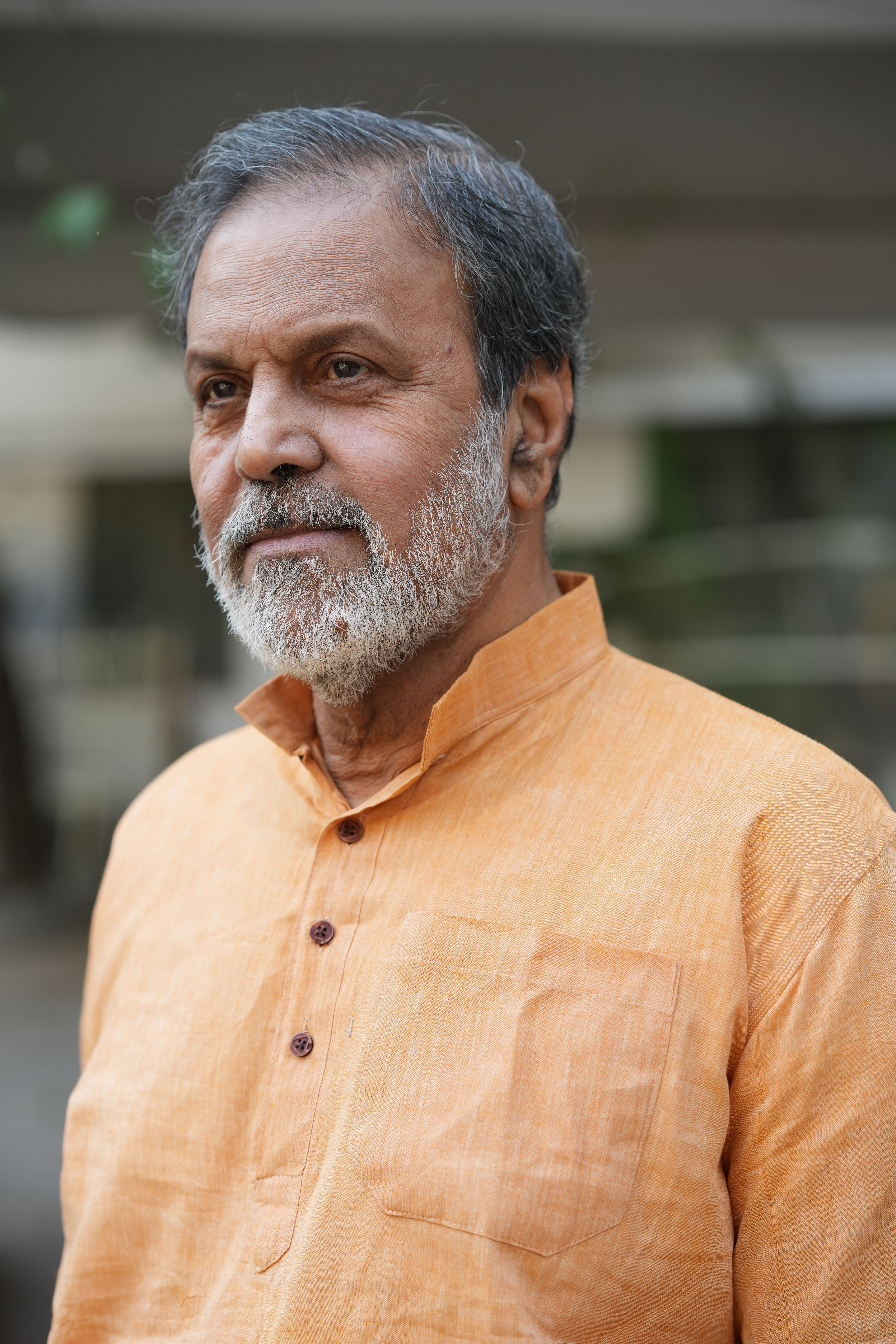 Elderly man wearing an orange kurta, captured outdoors with a thoughtful expression.