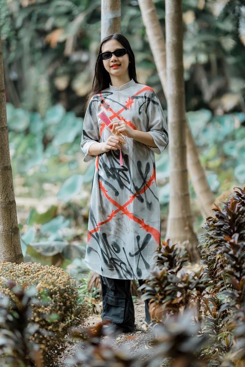 Free Stylish woman in a uniquely patterned dress enjoys a serene outdoor setting, surrounded by lush greenery. Stock Photo