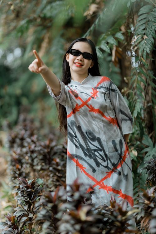 Free Fashionable young woman in a graffiti-style dress amidst lush greenery, showcasing trendy sunglasses. Stock Photo