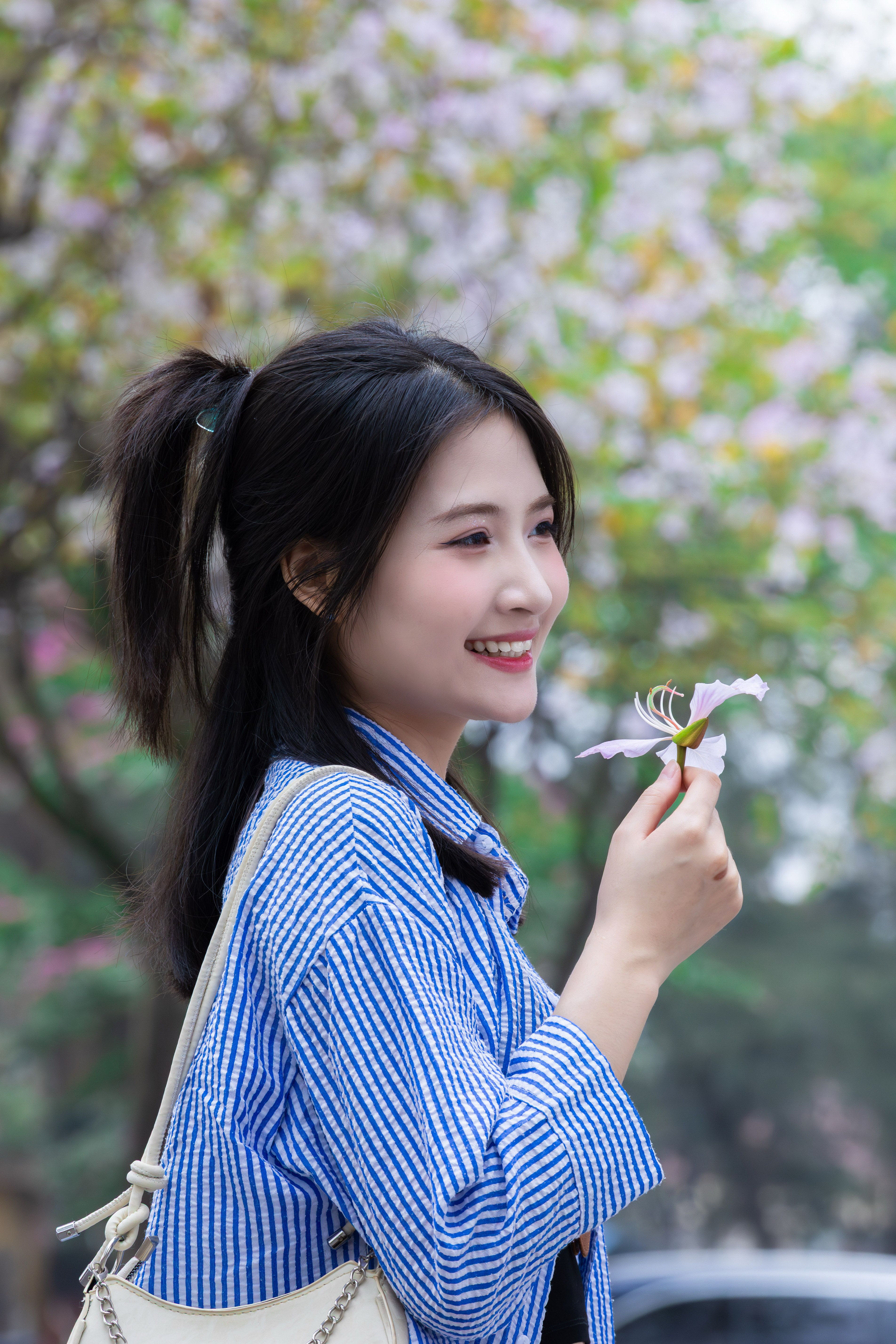 A young woman smiles while holding a flower, enjoying a spring day in Hanoi, Vietnam.