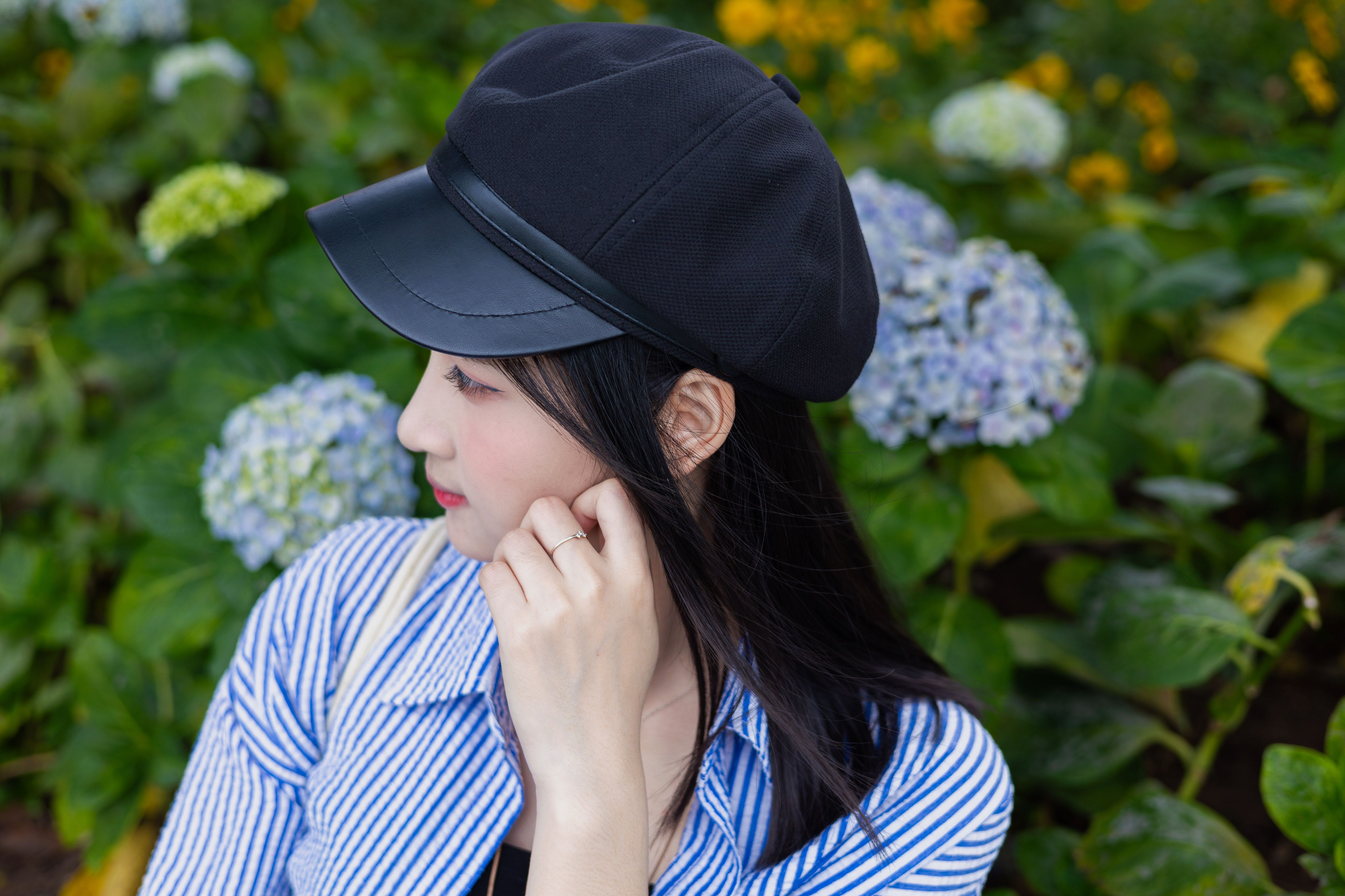 Portrait of a young woman in Hanoi garden, wearing a black cap, with vibrant hydrangeas in background.