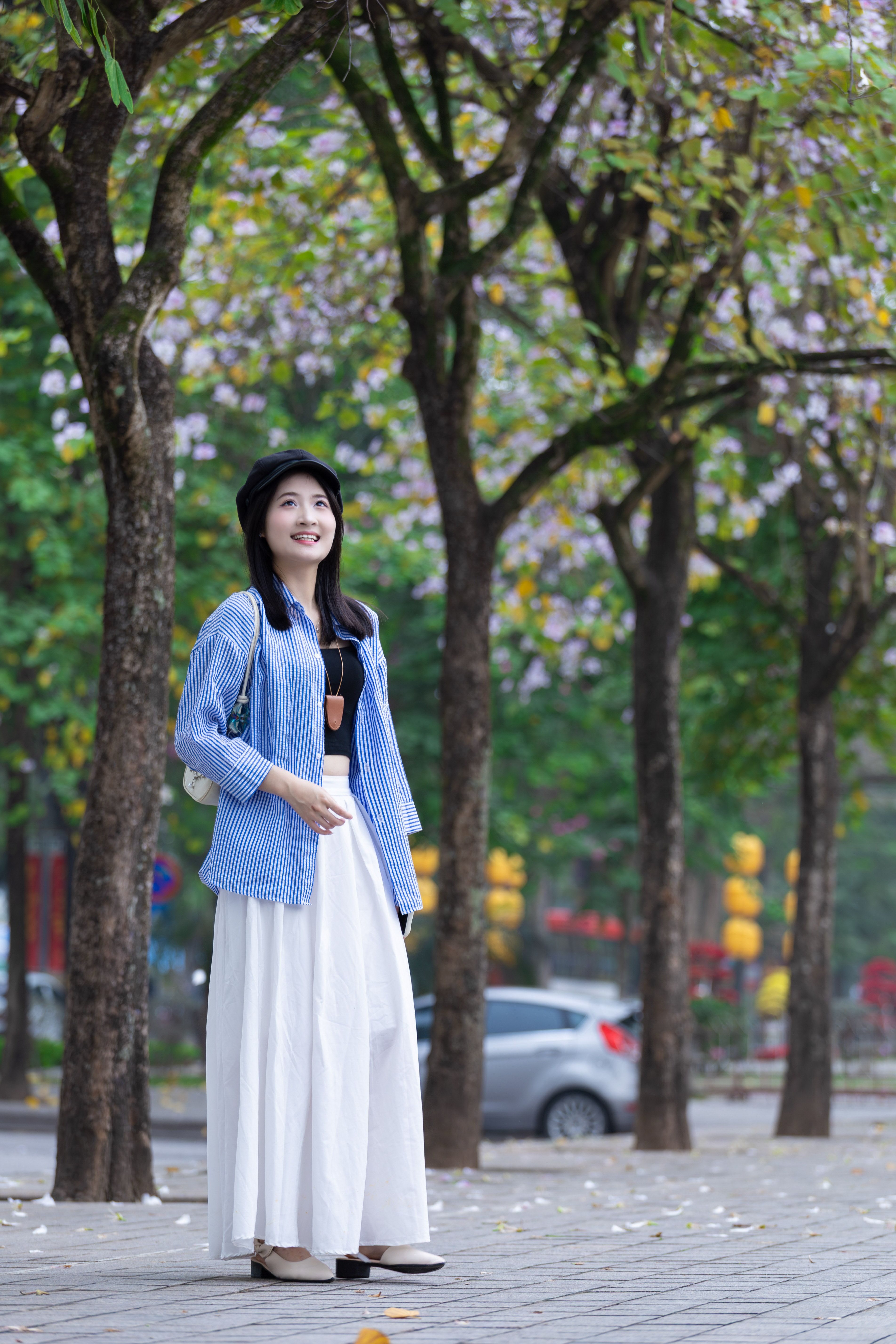 A woman in spring attire enjoys a peaceful walk under blooming trees in Hanoi, Vietnam.